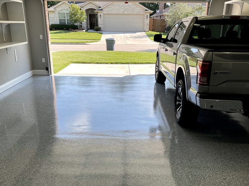 Two-car garage with a grey full-broadcast flake polyaspartic floor and a pickup parked at the open door